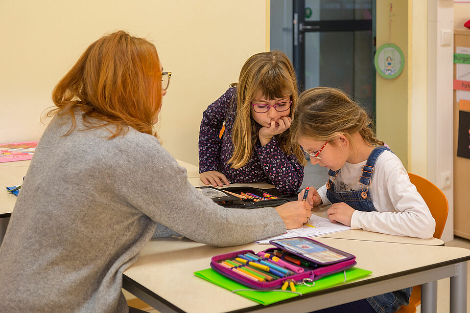 Frau hilft zwei Mädchen bei Schulaufgaben.