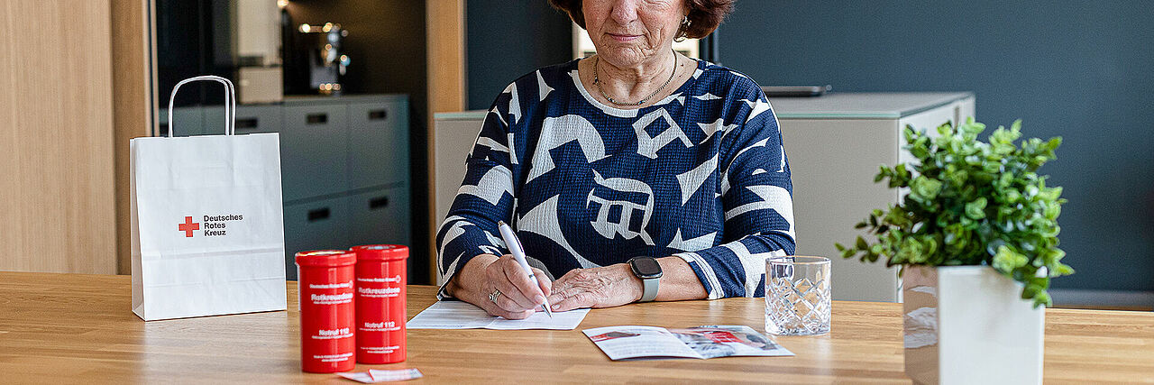 Ältere Frau mit einer Rotkreuzdose, in der wichtige persönliche und Gesundheitsdaten für den Notfall hinterlegt sind.