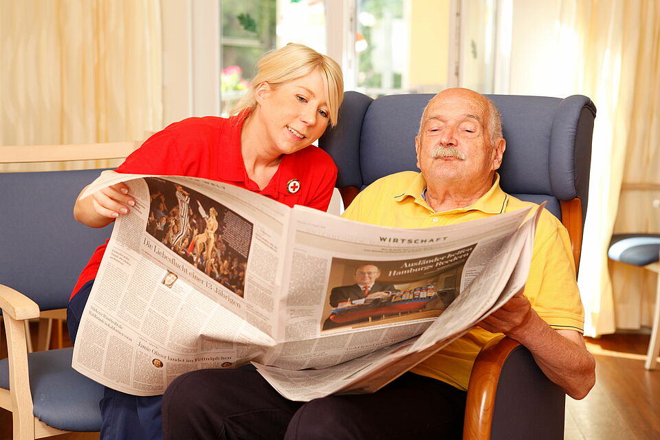 Eine Mitarbeiterin des DRK liest zusammen mit einem alten Herren die Zeitung.